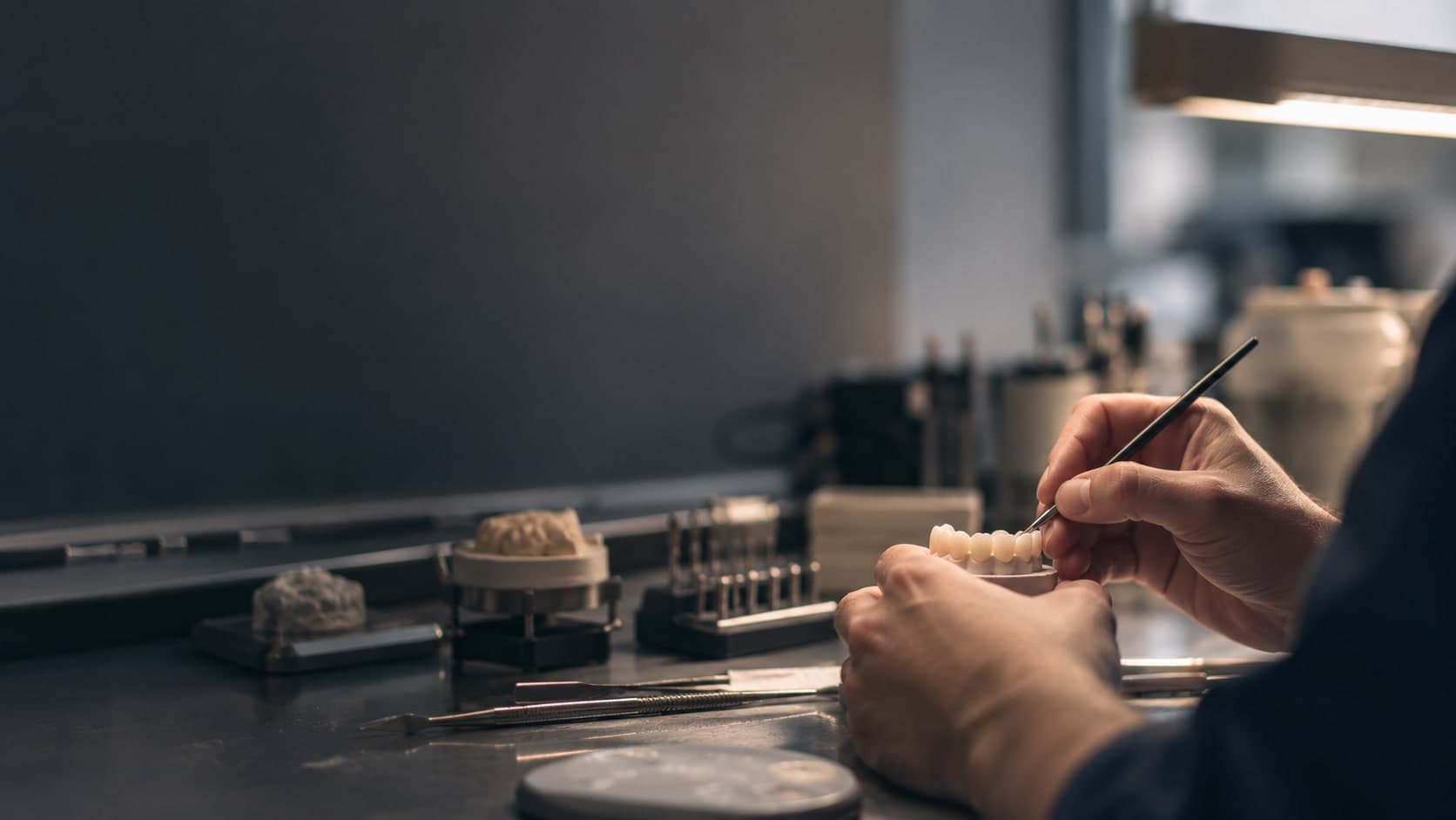 A dental technician brushing characterisation onto a ceramic bridge at the lab bench.
